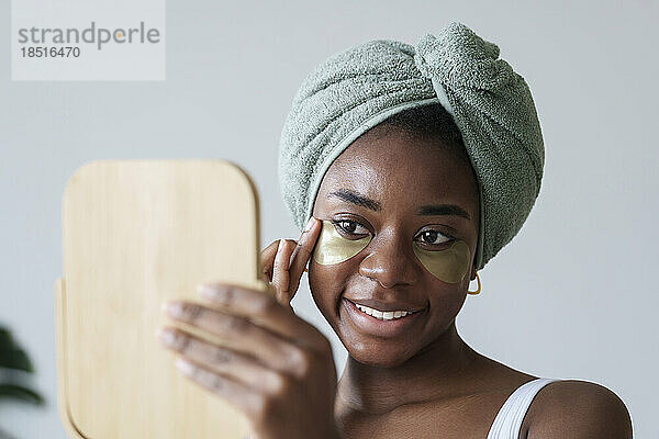 Lächelnde junge Frau mit Spiegel  die eine Augenklappe anbringt