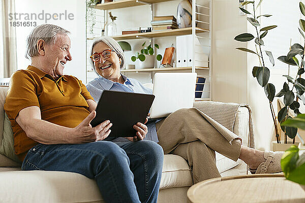 Glückliches älteres Paar sitzt mit Tablet-Computer auf dem Sofa im Wohnzimmer