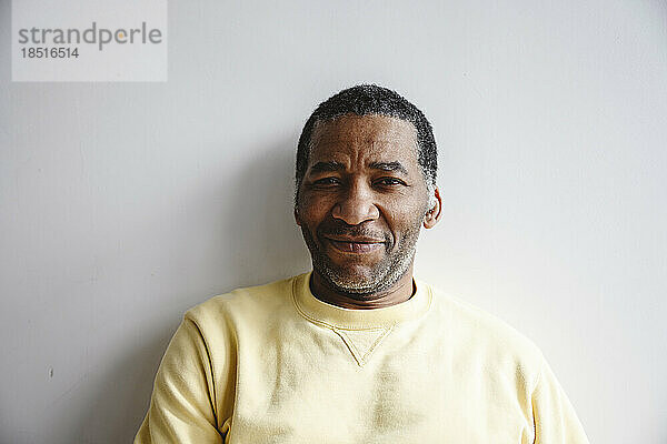 Smiling mature man leaning on white wall