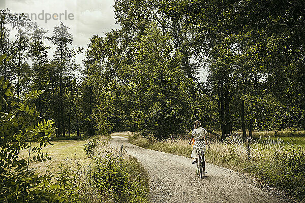 Frau fährt Fahrrad auf schmaler unbefestigter Straße