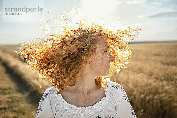 Happy redhead woman tossing hair in field