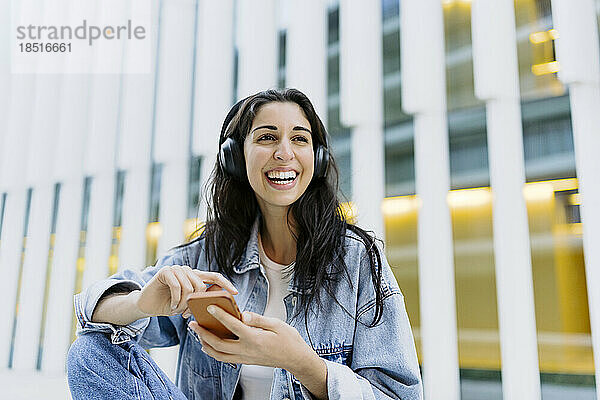 Glückliche junge Frau mit Smartphone vor dem Gebäude