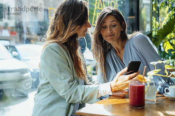 Frau teilt Smartphone mit Freund im Café