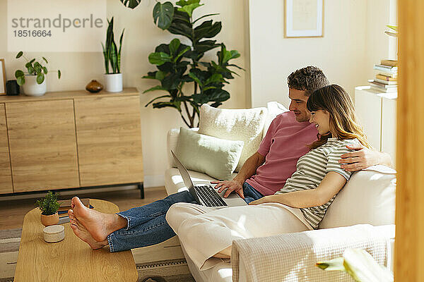 Freund mit Arm um Freundin und Laptop auf Sofa im Wohnzimmer