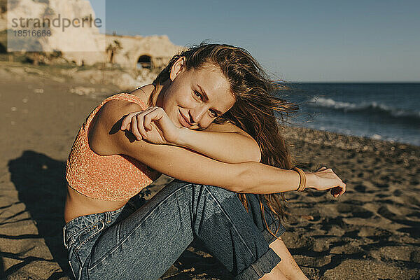 Lächelnde Frau sitzt an einem sonnigen Tag am Strand