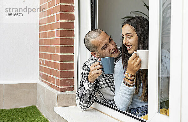 Glückliches Paar beim Kaffeetrinken am Fenster zu Hause