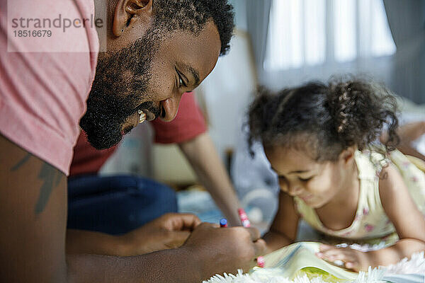 Glücklicher Mann macht mit seiner Tochter zu Hause eine Skizze