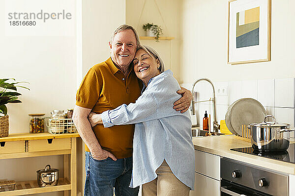 Happy senior woman embracing man in kitchen