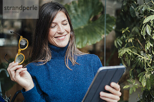 Glückliche Geschäftsfrau mit Tablet-PC vor Glaswand