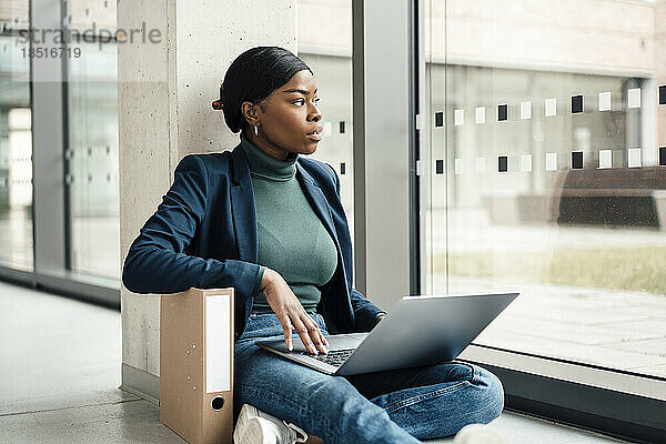 Nachdenkliche Geschäftsfrau mit Laptop sitzt im Büro