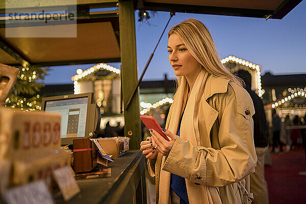 Junge Frau mit Smartphone bestellt Essen am Imbissstand