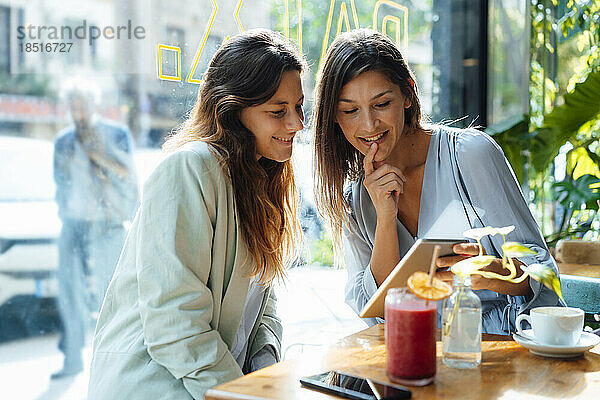 Lächelnde Frauen teilen sich Tablet-PC im Café