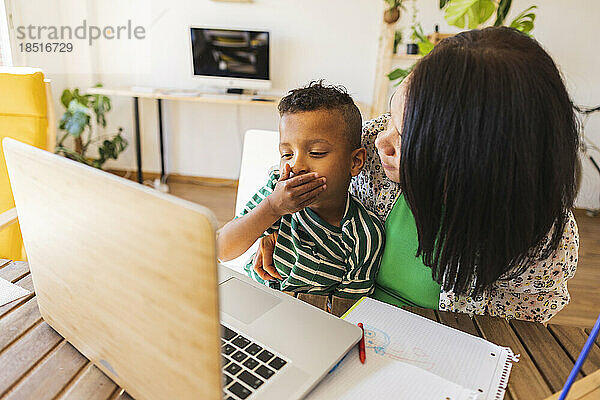 Boy covering mouth with mother watching laptop at home