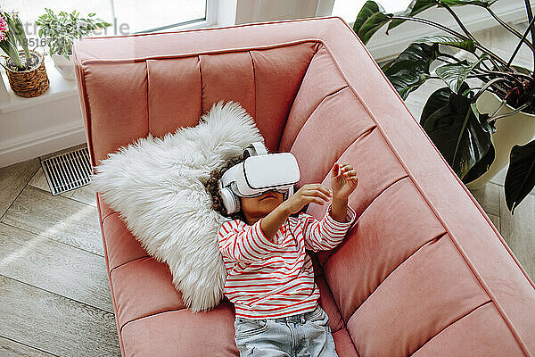 Mädchen mit Virtual-Reality-Simulator gestikuliert und liegt auf dem Sofa