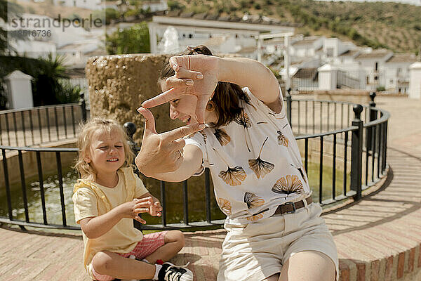 Glückliche Mutter macht an einem sonnigen Tag einen Fingerrahmen mit ihrer Tochter