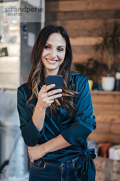 Glückliche Geschäftsfrau steht mit Smartphone im Büro