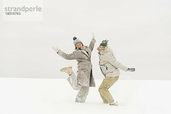 Sorglose Freunde tanzen im Winter gemeinsam im Schnee