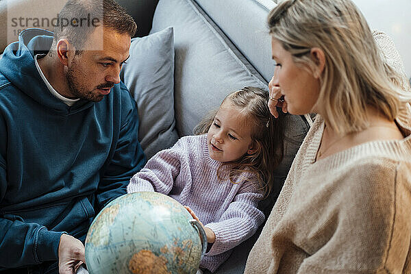Tochter und Eltern schauen zu Hause auf dem Sofa auf den Globus