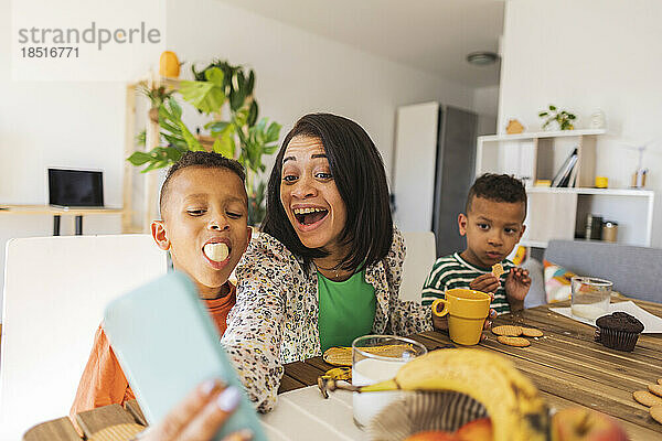 Fröhlicher Junge frühstückt und macht zu Hause ein Selfie mit der Familie