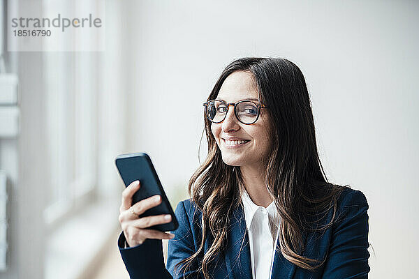 Lächelnde Geschäftsfrau hält Smartphone im Heimbüro