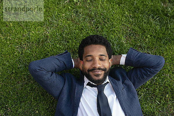 Smiling businessman with eyes closed relaxing on grass