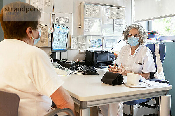 Arzt bespricht sich mit älterem Patienten  der am Schreibtisch in der Klinik sitzt