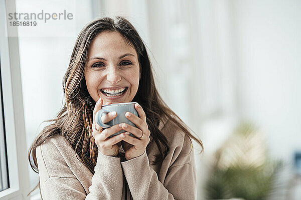 Glückliche junge Frau hält Kaffeetasse zu Hause