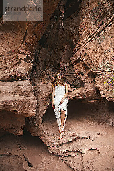 Frau lehnt auf Felsen in roter Sandhöhle