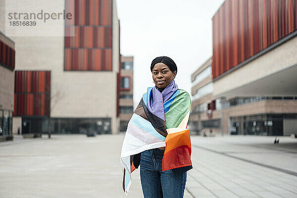 Junge Frau mit Regenbogenfahne bedeckt steht vor dem Gebäude