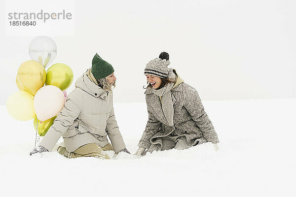 Glückliche Frauen mit Luftballons genießen den Schnee