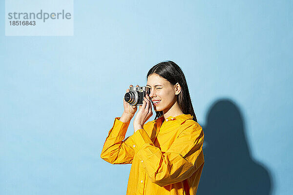 Young woman clicking photo through camera against colored background