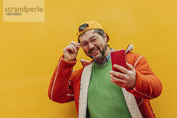 Glücklicher reifer Mann  der ein Selfie vor farbigem Hintergrund macht
