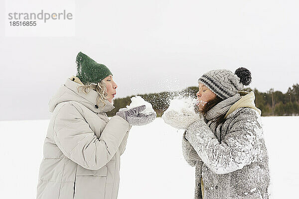Frauen mit Strickmützen blasen sich gegenseitig mit Schnee an