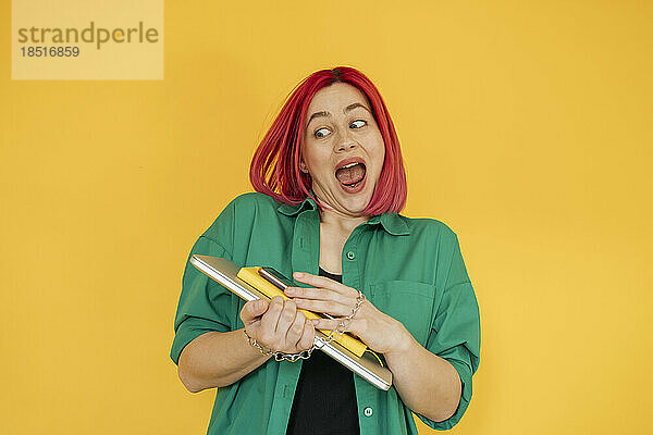 Happy woman with dyed hair holding laptop over yellow background