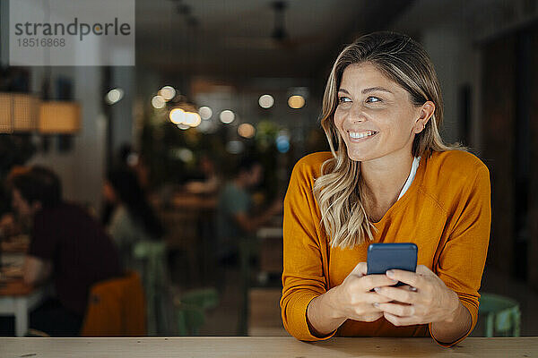 Nachdenkliche  glückliche Frau mit Smartphone sitzt im Café