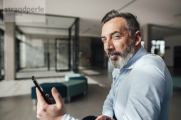 Lächelnder Geschäftsmann mit Smartphone im Büro