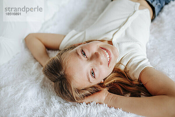 Fröhliches Mädchen entspannt sich zu Hause auf dem Fellbett