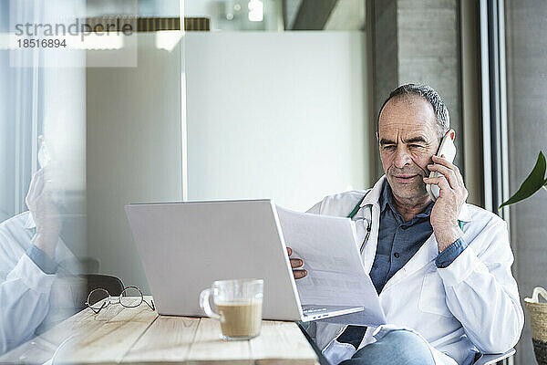 Arzt untersucht ärztlichen Bericht und diskutiert am Schreibtisch auf dem Smartphone