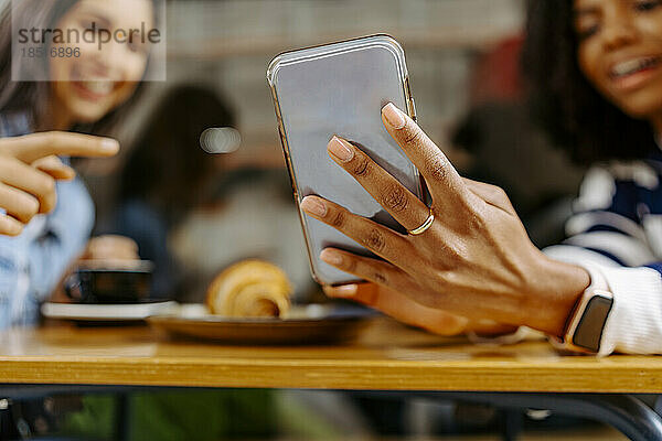 Junge Frau zeigt einem Freund im Café ihr Smartphone