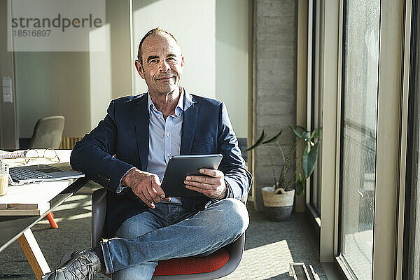 Selbstbewusster reifer Geschäftsmann sitzt mit Tablet-PC im Büro