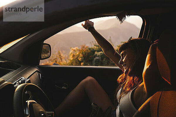 Glückliche junge Frau genießt den Sonnenuntergang im Auto