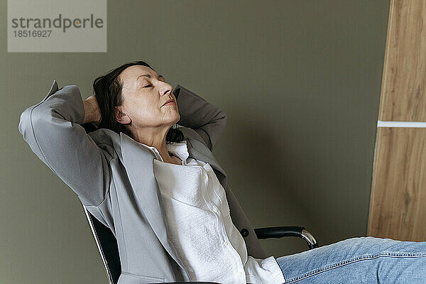 Tired businesswoman relaxing with hands behind head at office