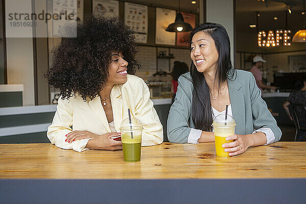 Smiling multiracial friends with juice sitting at cafe