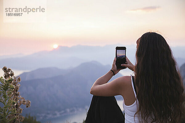 Junge Frau fotografiert Sonnenuntergang per Smartphone