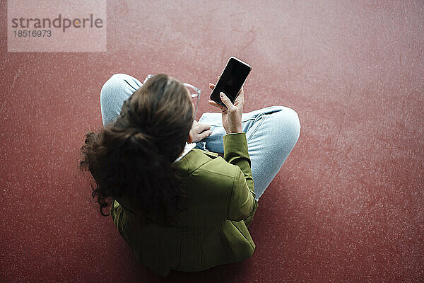 Geschäftsfrau sitzt mit Smartphone auf dem Boden
