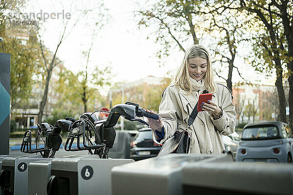 Frau benutzt Smartphone und steht neben Fahrrad am Parkplatz