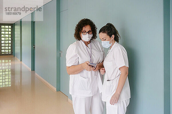 Ärzte teilen sich ihr Smartphone und stehen auf dem Flur des Krankenhauses