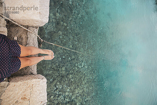 Frau sitzt barfuß am Meer