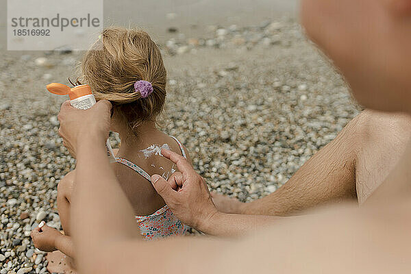 Mann trägt Sonnencreme auf Tochter am Strand auf