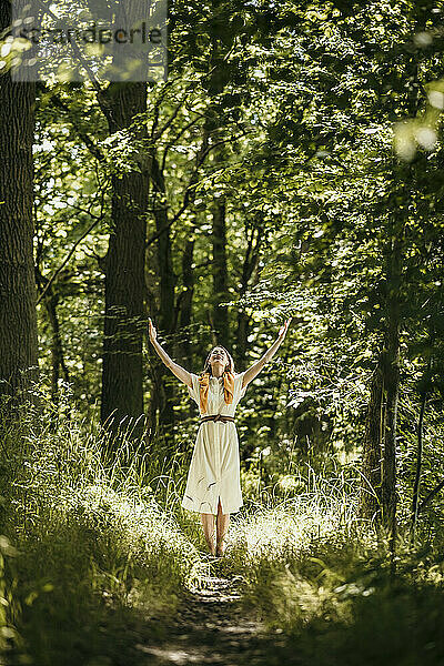 Frau mit erhobenen Händen steht an einem sonnigen Tag im Wald